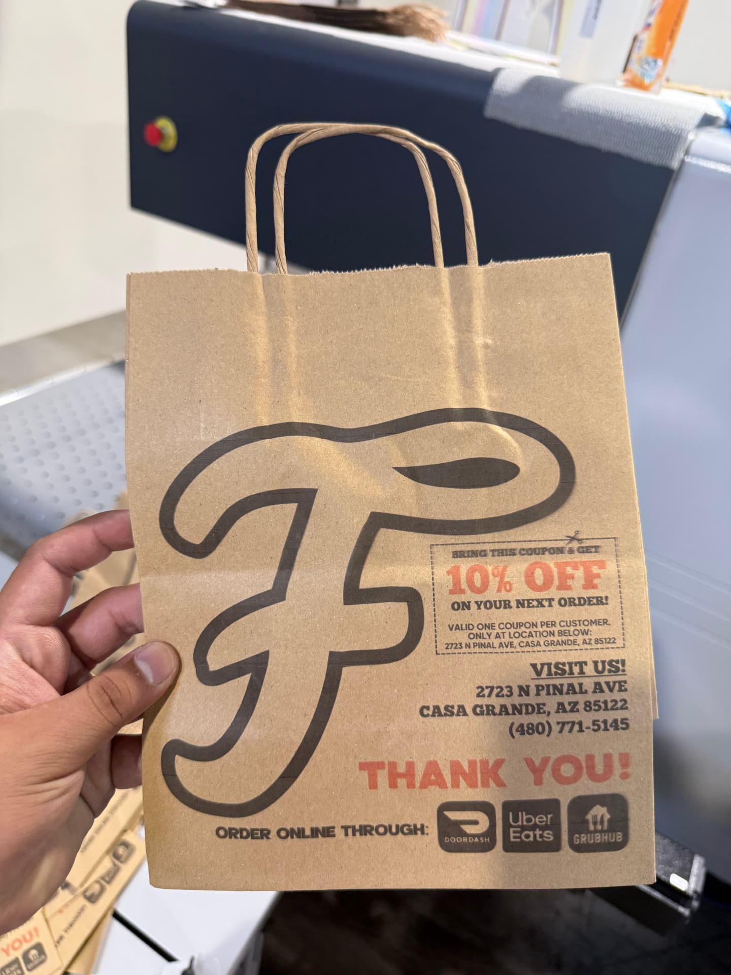 Small kraft takeout bag with handles printed with a script F logo and a 10% off coupon
